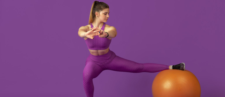 Shape. Beautiful young female athlete practicing in studio, monochrome purple portrait. Sportive caucasian fit model training with fitball. Body building, healthy lifestyle, beauty and action concept.